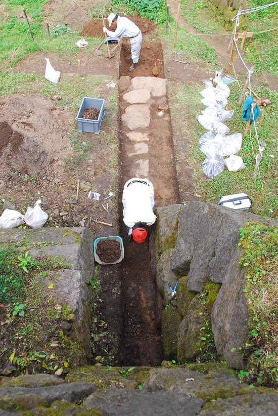 狭い溝の中を手作業で掘る発掘調査現場の風景