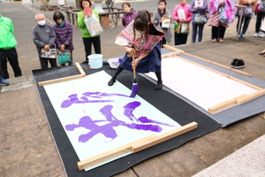 物部神社で見学者に囲まれる中　共創を書く井上さん