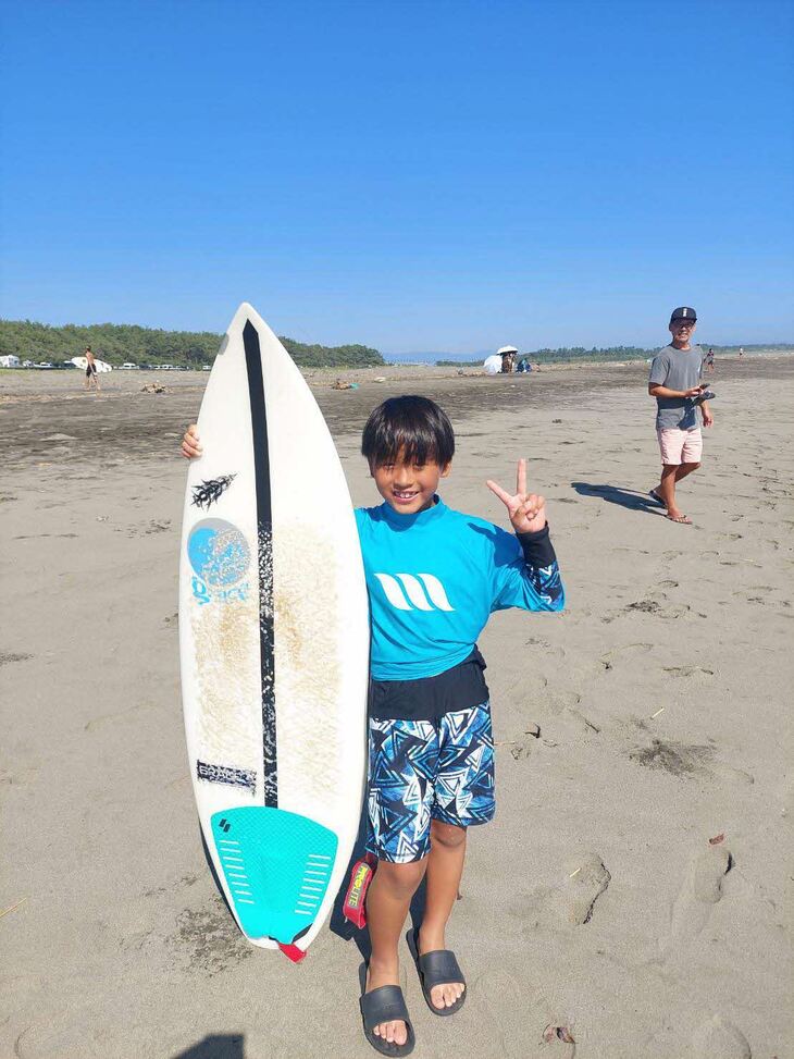 海をバックにボードを持つ秀豪さん