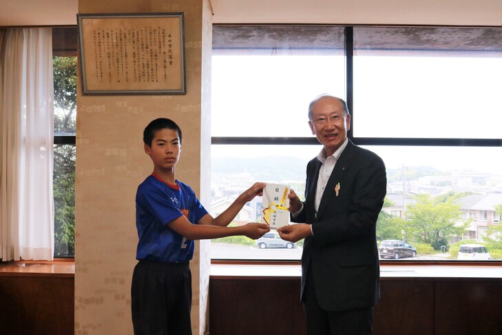 激励金を手渡す市長と受け取る山﨑さん